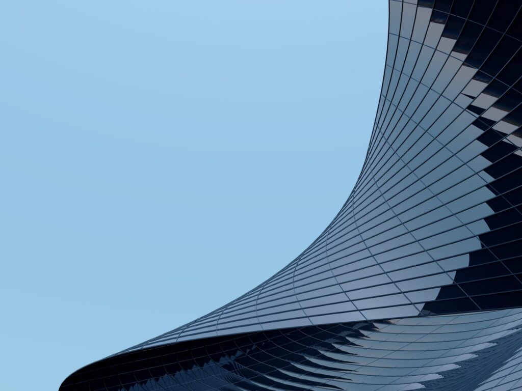 A curved glass tower sweeping against a pale blue sky.