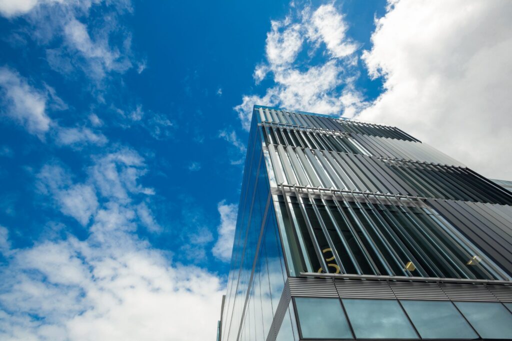 A glass office tower with louvred fins, seen from below against a cloudy sky.